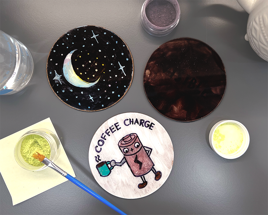 three thermochromic coasters, each with different designs (moon, black, and coffee battery)